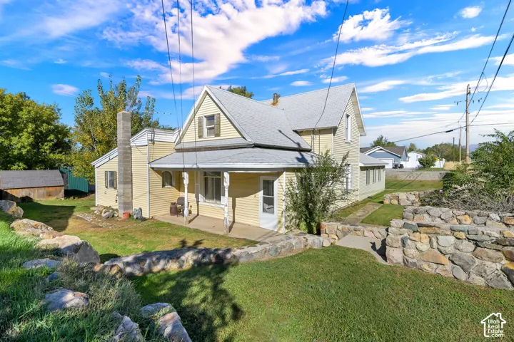 Two-story residence with yellow horizontal siding, a covered porch, a stone exterior chimney, and tiered natural stone retaining walls