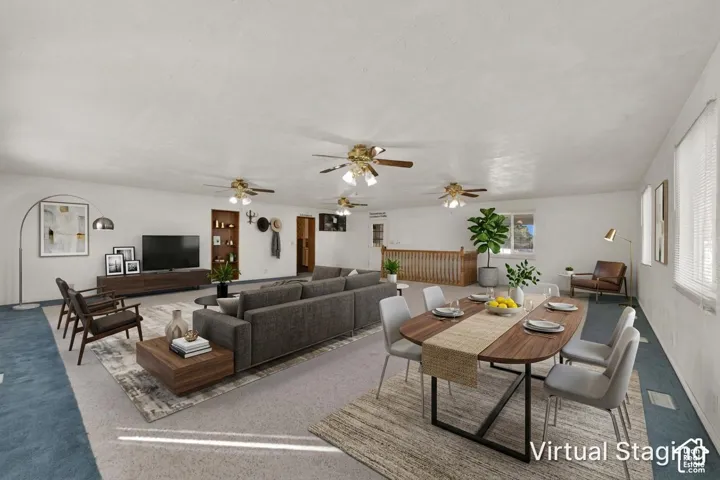 Open-concept interior featuring wall-to-wall carpeting, three ceiling-mounted light fixtures with paddle fans, built-in recessed shelving, and a wooden balustrade