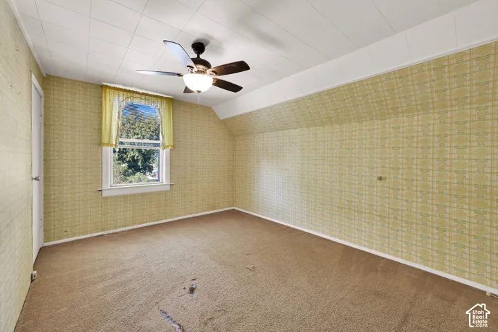 Room featuring vaulted ceilings, carpeted flooring, a ceiling fan with integrated lighting, and a single-pane window