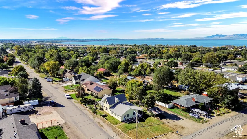 Aerial perspective of the property featuring a detached residence with solar panels, a grass lawn, and expansive surroundings including a nearby lake and mountain backdrop