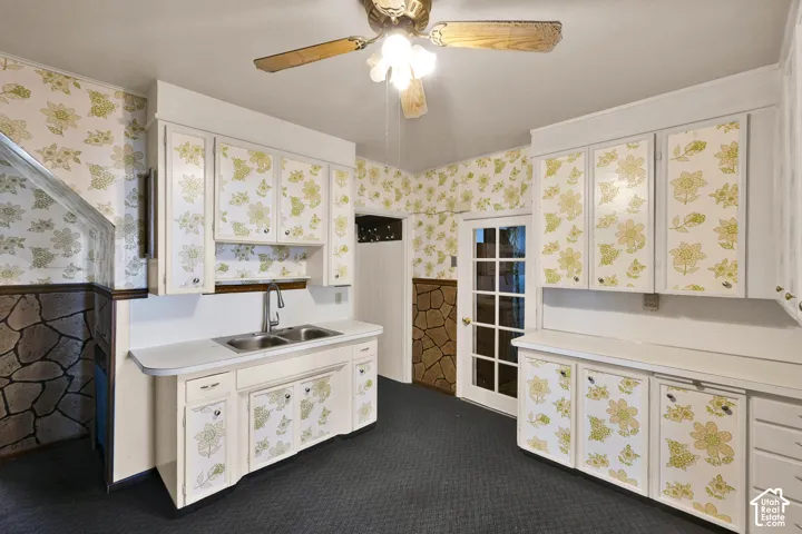 Kitchen featuring custom cabinetry with floral-patterned inserts, double-basin stainless steel sink with high-arc faucet, stone-finish wainscoting, and a multi-pane glass door