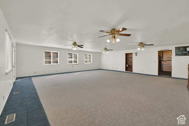 Expansive interior space featuring neutral carpeting, multi-light ceiling fans, recessed wall shelving, and multiple windows