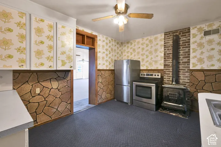 Kitchen featuring stone-finish wall cladding, a metal wood-burning stove with exposed brick backing, stainless steel appliances, and built-in cabinetry