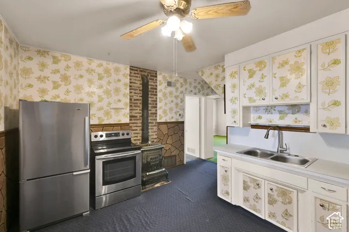 Kitchen featuring stainless steel refrigerator and range, integrated wood-burning stove with stone masonry surround, double-basin stainless steel sink, and ceiling-mounted fan