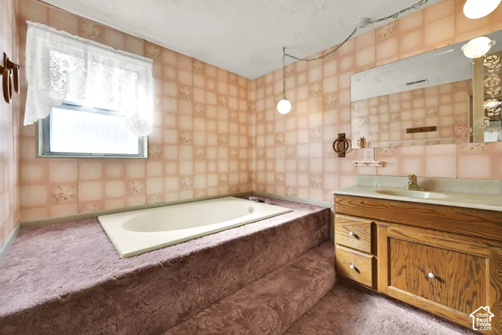 Built-in deep soaking tub set within a raised platform, wood-finish vanity cabinet, integrated countertop basin, and wall-mounted light fixtures