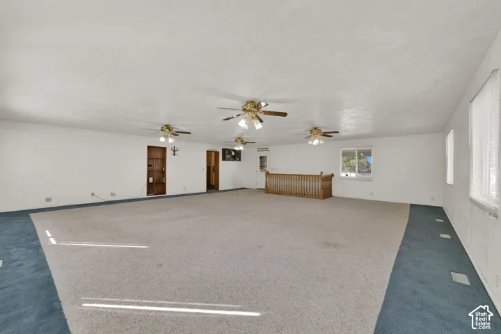 Expansive room featuring wall-to-wall carpeting, three ceiling fans with integrated lighting, built-in shelving, and wood railing