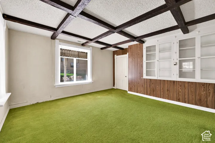 Coffered ceiling featuring dark wood-finish beams, built-in cabinetry with glass-front doors, and wood-finish wall paneling