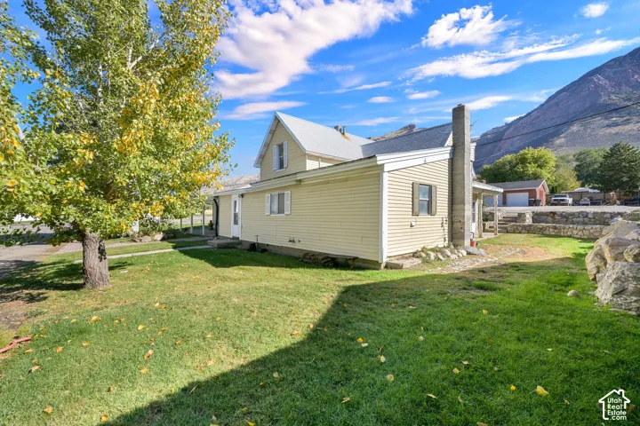 Exterior of the residence featuring horizontal siding, a pitched metal roof, an external masonry chimney, and stone retaining walls, set against a mountainous backdrop