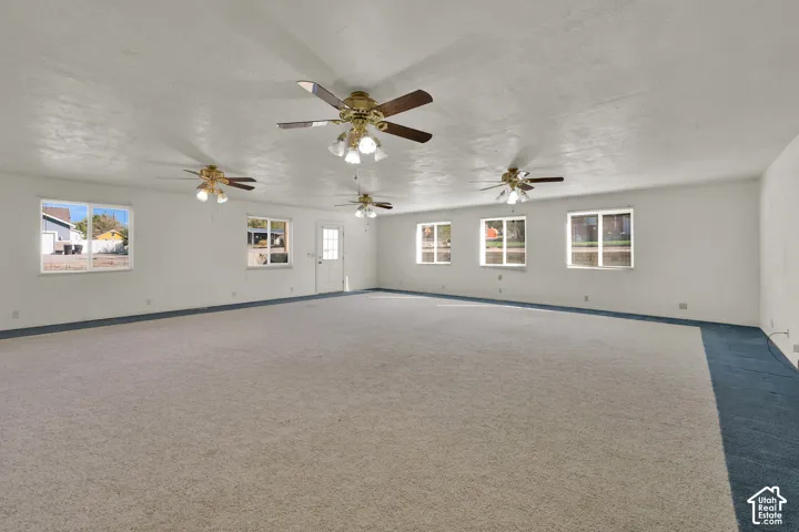 Expansive room featuring wall-to-wall carpeting, multiple ceiling fans with integrated lighting, and six double-pane windows