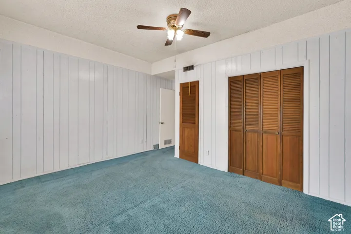 Room featuring vertical paneling, textured ceiling, ceiling fan with integrated lighting, and wooden louvered closet doors
