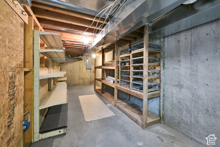 Unfinished storage area featuring exposed wood ceiling joists, concrete foundation walls, poured concrete flooring, and built-in wood-frame shelving