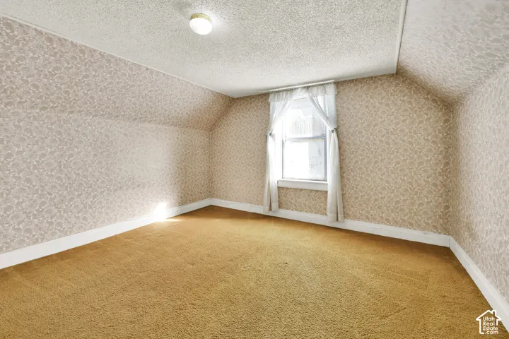 Interior space featuring patterned wallpaper, carpeted flooring, sloped ceilings, and a single window with decorative trim