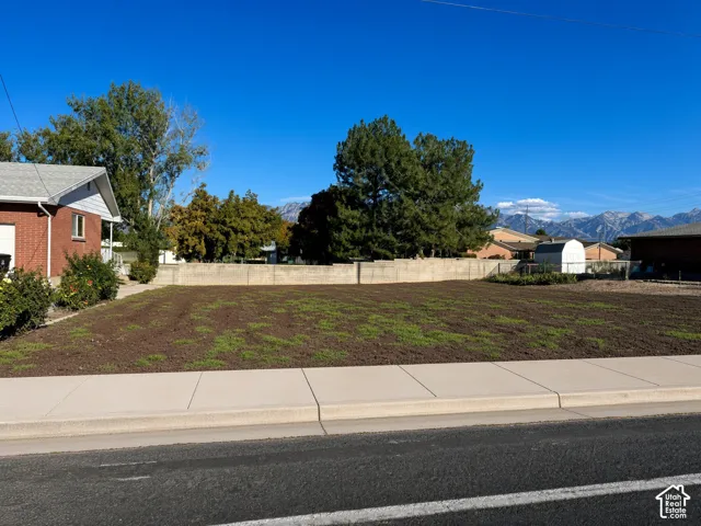 Open lot featuring concrete curbing, a concrete sidewalk, a perimeter block wall, and mountain backdrops