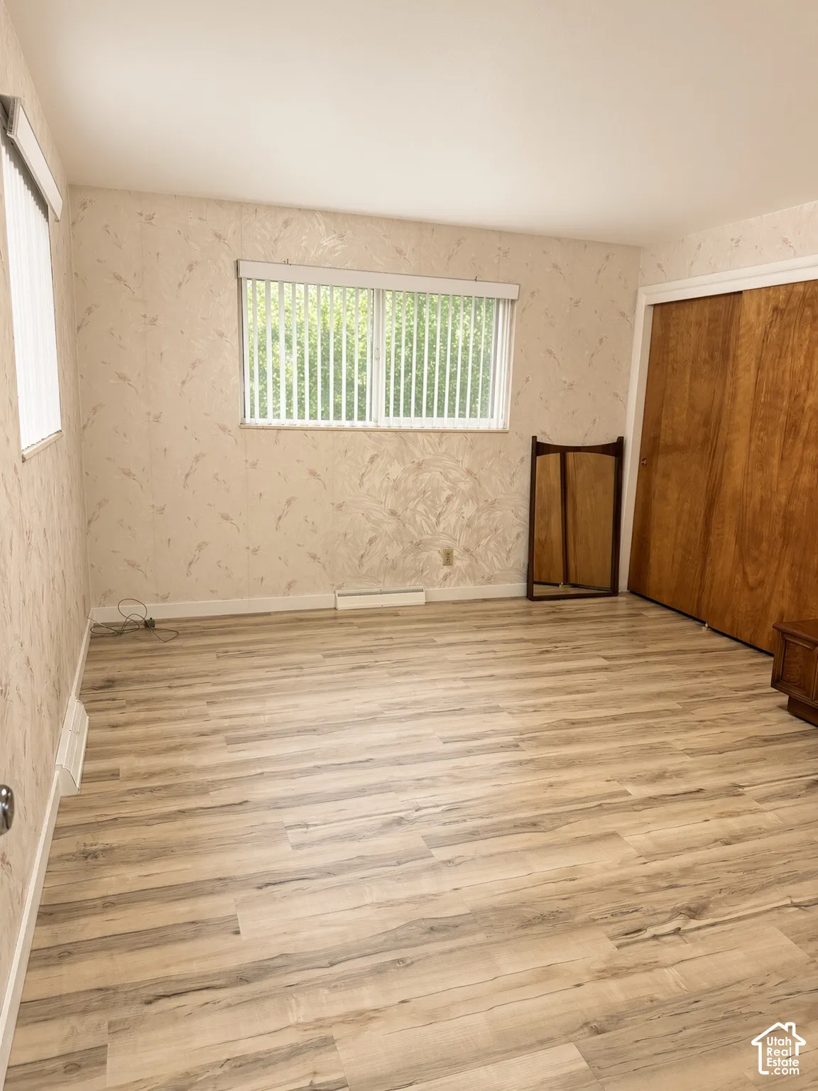 Interior room featuring light wood-finish flooring, patterned wallpaper, horizontal window blinds, and wood-panel sliding closet doors