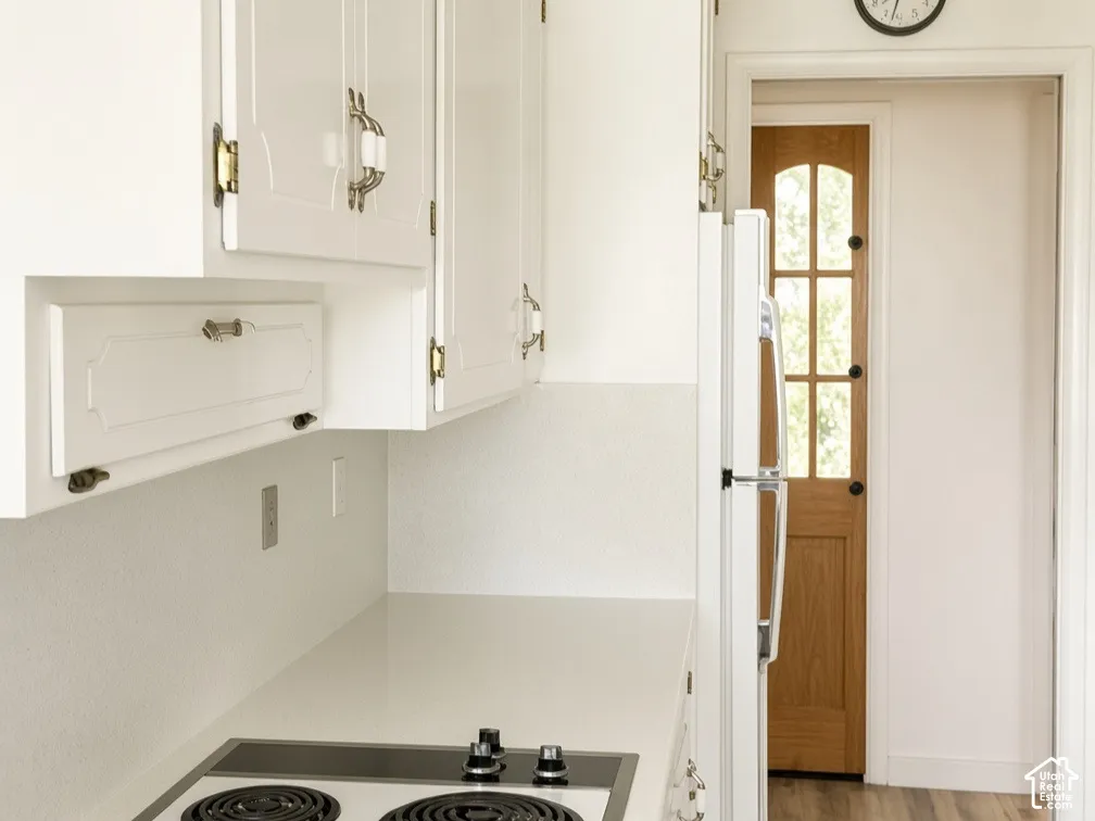 White cabinetry with brass-finish hardware, solid-surface countertop, electric cooktop, and wood-finish flooring