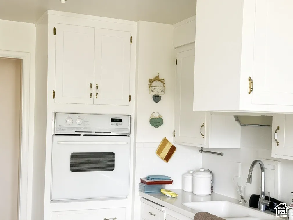 Kitchen featuring white cabinetry, built-in wall oven, solid-surface countertops, dual-basin sink with gooseneck faucet, and wood-finish flooring