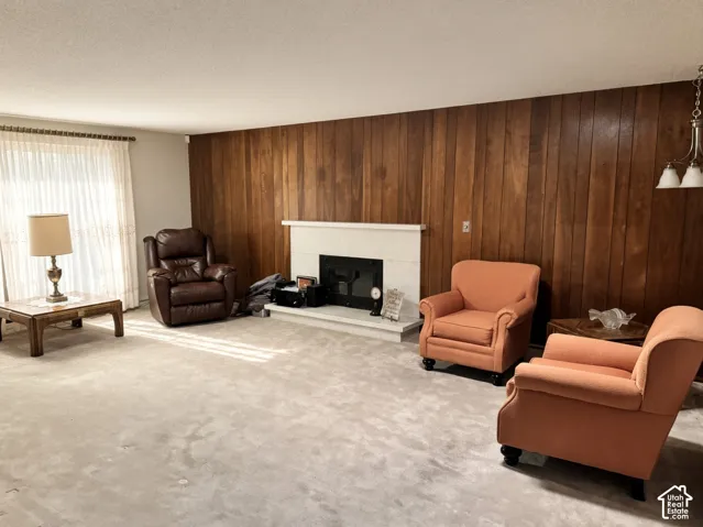 Wood-panelled accent wall featuring a light-toned fireplace surround and hearth, carpeted flooring, and a multi-light pendant fixture