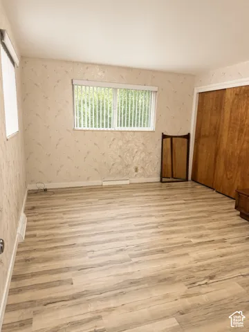 Interior room featuring light wood-finish flooring, patterned wallpaper, horizontal window blinds, and wood-panel sliding closet doors