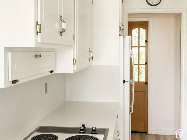 White cabinetry with brass-finish hardware, solid-surface countertop, electric cooktop, and wood-finish flooring