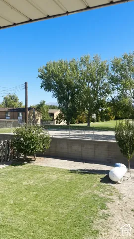 Outdoor space featuring a concrete retaining wall, chain-link fencing, mature trees, and a level lawn