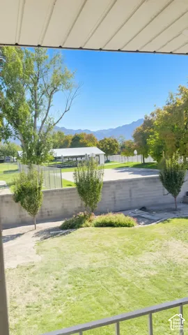 Backyard featuring a manicured lawn, concrete retaining wall, mature trees, and a mountain backdrop