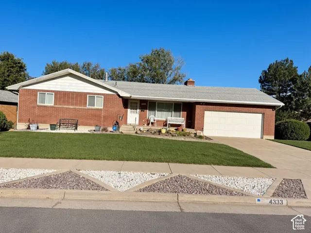 Single-story brick exterior featuring a low-pitched roofline, two-car garage, and landscaped front yard with decorative stone accents