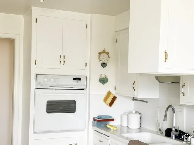 Kitchen featuring white cabinetry, built-in wall oven, solid-surface countertops, dual-basin sink with gooseneck faucet, and wood-finish flooring
