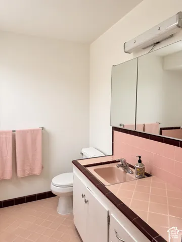 Bathroom featuring a vanity with integrated sink, tiled countertop with contrasting border, built-in medicine cabinet, and tiled flooring