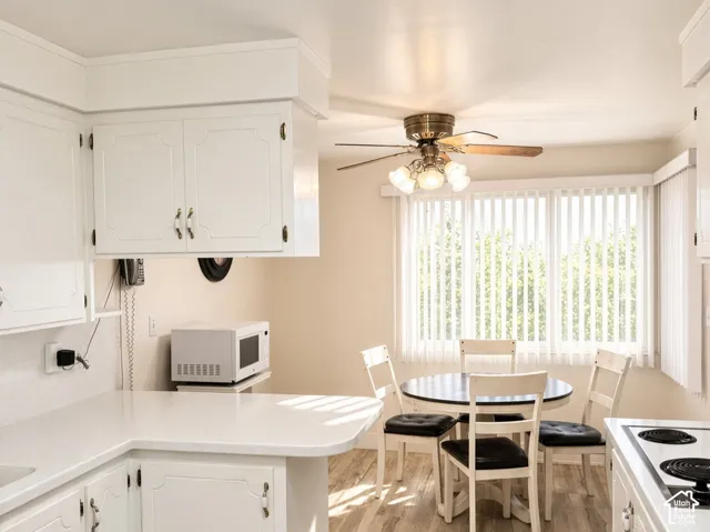 Kitchen featuring white cabinetry, solid-surface countertops, wood-finish flooring, a ceiling fan with integrated lighting, and vertical window blinds