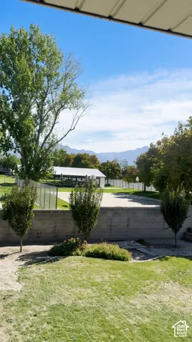 Backyard featuring a concrete retaining wall, manicured lawn, mature trees, and a mountain backdrop