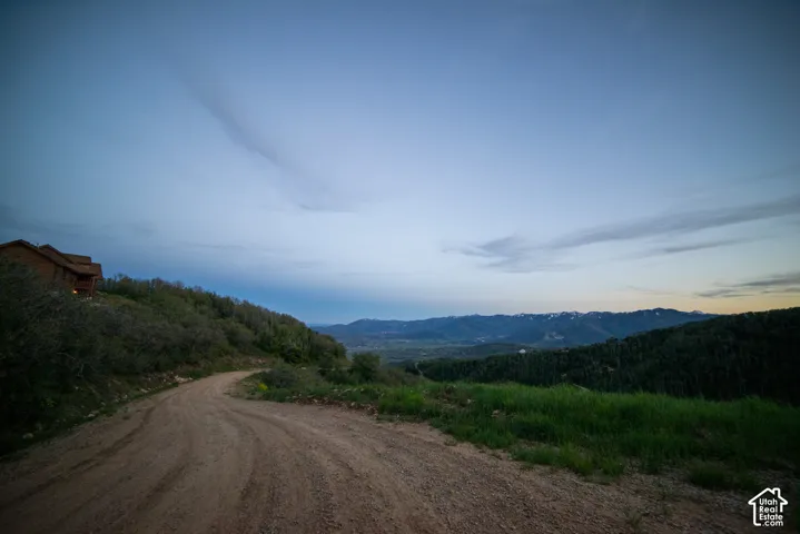 Expansive mountain scenery and rolling hillside landscape featuring a rustic timber-clad structure and an unpaved access road