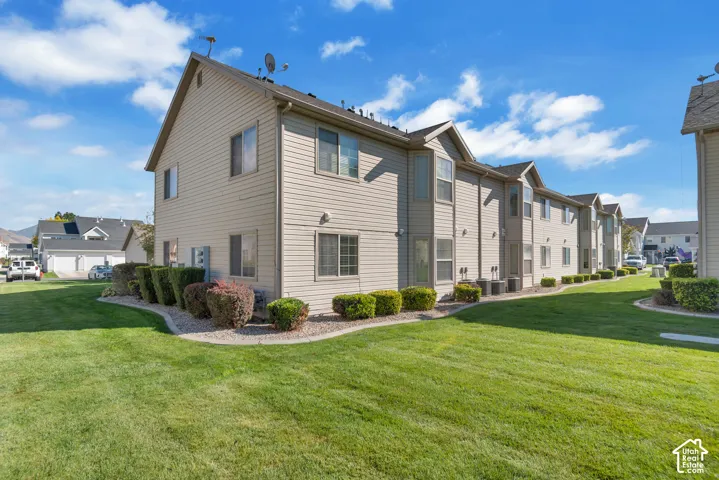 Multi-story exterior featuring tan horizontal siding, gabled rooflines, double-pane windows, and manicured turf landscaping with stone-mulched garden beds