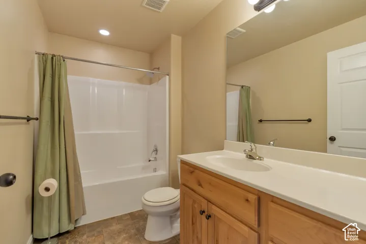 Full bathroom featuring a wood-finish vanity with a solid-surface countertop, an integrated sink, a large wall-mounted mirror, and a combination tub and shower enclosure with a surround