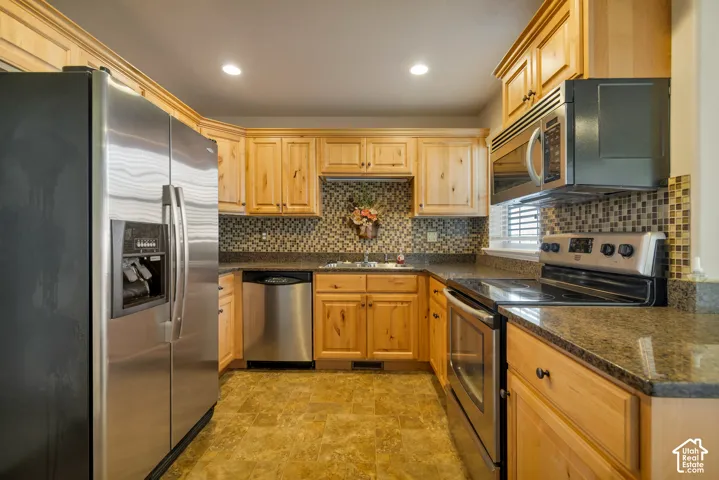 Kitchen featuring natural wood cabinetry, stone countertops, stainless steel appliances, and a mosaic tile backsplash