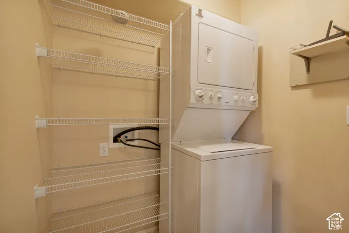 Laundry area featuring a stackable washer and dryer unit, white wire shelving, and a wall-mounted storage shelf