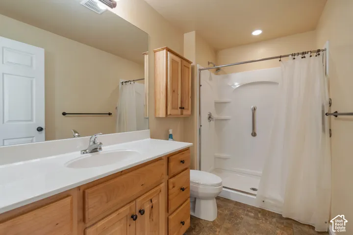Bathroom featuring a wood-finish vanity with a solid-surface countertop, an integrated sink, an overhead wall-mounted storage cabinet, a full-width vanity mirror, and a walk-in shower enclosure