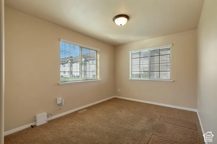 Neutral-toned room featuring neutral wall-to-wall carpeting, dual windows with horizontal blinds, and a circular flush-mount ceiling light fixture