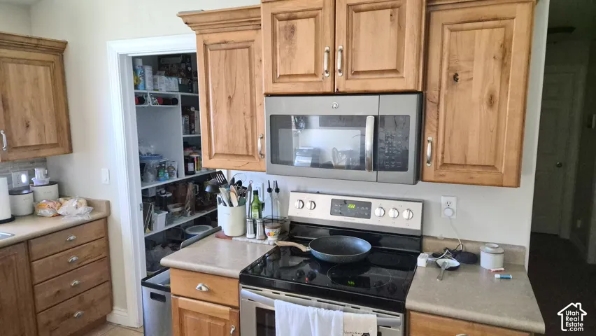 Kitchen featuring natural wood cabinetry, solid surface countertops, stainless steel electric range, built-in microwave, and walk-in pantry with integrated shelving
