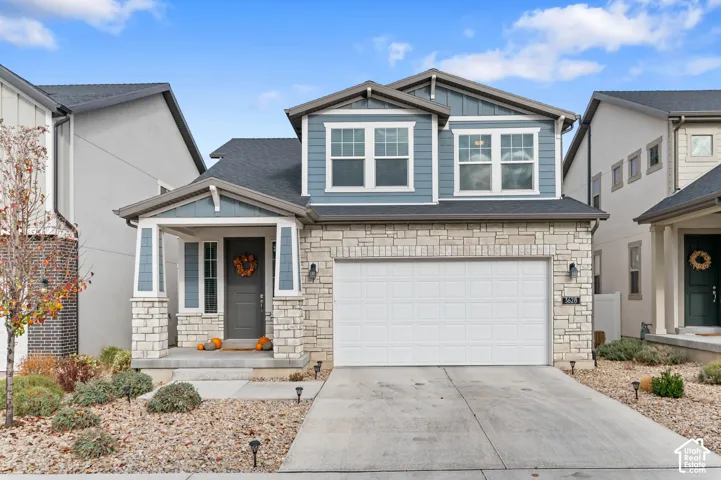 Two-story exterior featuring stone veneer siding, horizontal lap siding accents, covered front entryway, attached two-car garage, and asphalt shingle roof