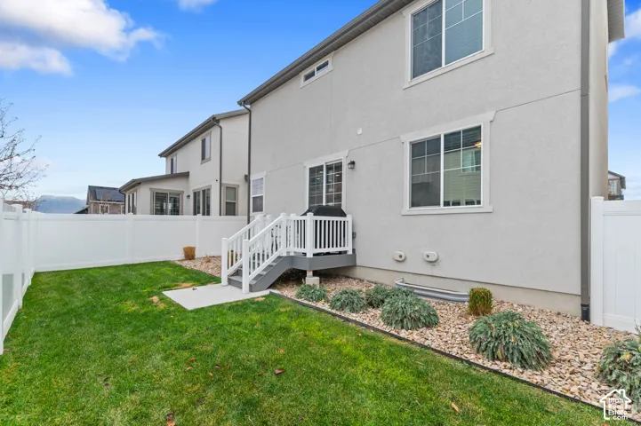 Stucco exterior featuring a raised deck with white railings, a fully fenced rear yard, low-maintenance gravel landscaping, and sliding glass entry doors