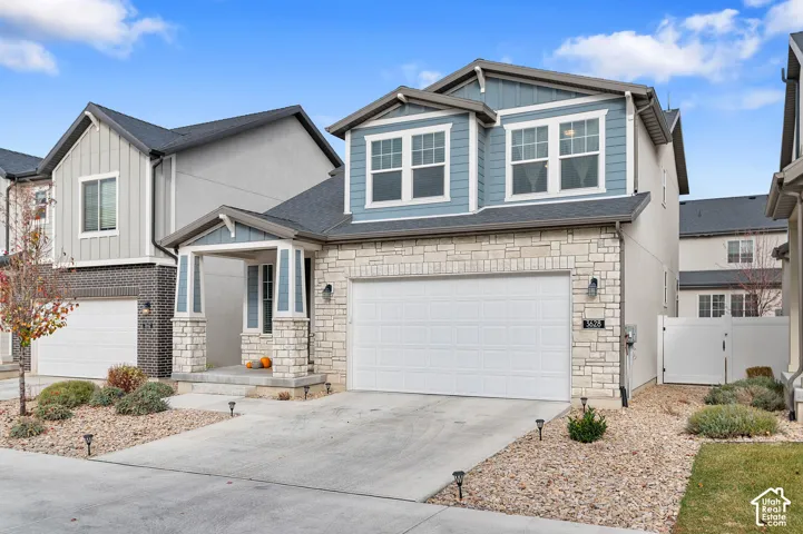Two-story exterior featuring a mix of horizontal siding and stone veneer, a covered front entryway with stone-column supports, a two-car garage, and xeriscaped front yard landscaping