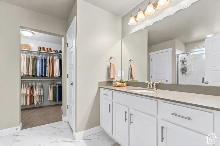 Bathroom featuring a white vanity cabinet with quartz countertops, undermount sink, multi-light fixture, and tile flooring, including access to a walk-in closet with built-in shelving