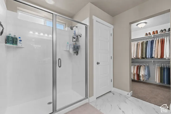 Walk-in shower with a glass enclosure and white surround, large-format tile flooring, and a walk-in closet featuring built-in shelving