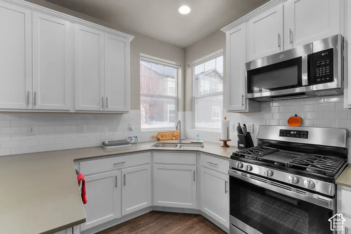 Kitchen featuring white cabinetry, quartz countertops, a white subway tile backsplash, stainless steel gas range with built-in microwave, and wood-finish flooring
