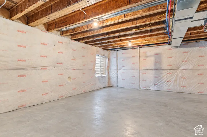Unfinished lower level featuring exposed wood joist ceilings, concrete flooring, insulated perimeter walls, and a recessed window