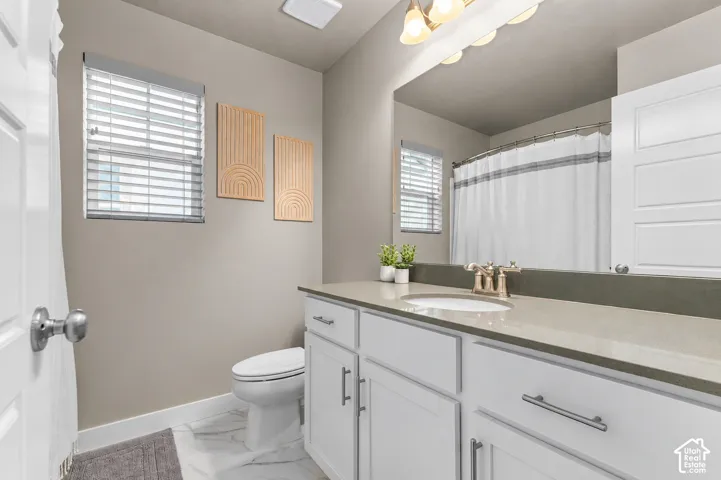Bathroom featuring a white vanity cabinet, solid surface countertop, drop-in sink with a metallic finish faucet, large vanity mirror, and neutral wall tones
