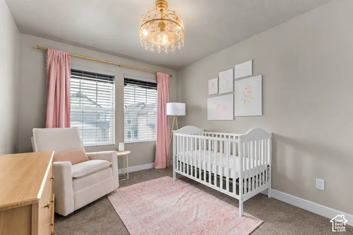 Room featuring neutral wall tones, plush carpeting, dual windows with integrated blinds, and an ornate gold-finish chandelier with crystal accents