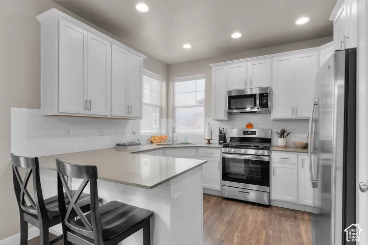 Kitchen featuring white cabinetry, solid surface countertops, a white subway tile backsplash, stainless steel appliances, and wood-finish flooring