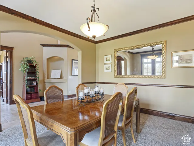Dining room featuring crown molding, chair rail, arched entryway, built-in wall niche, and an integrated pendant light fixture