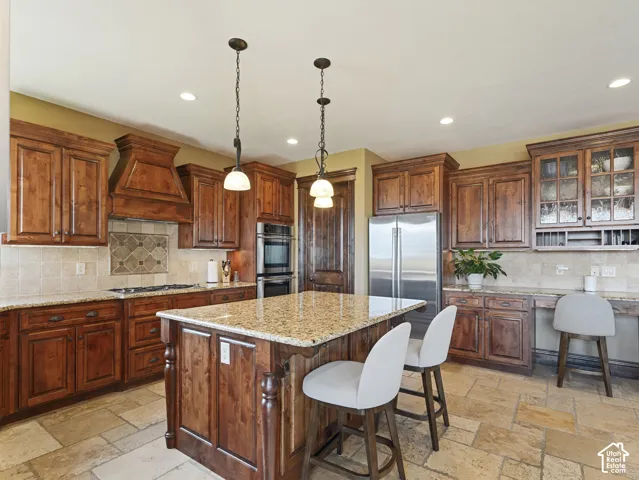 Kitchen featuring stained wood cabinetry, stone countertops, a central island with decorative corbels, natural stone tile flooring, and integrated stainless steel double wall ovens